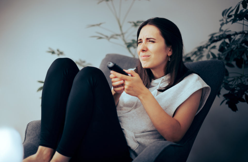 Woman sitting on couch with tv remote in hand squinting her eyes to be able to see