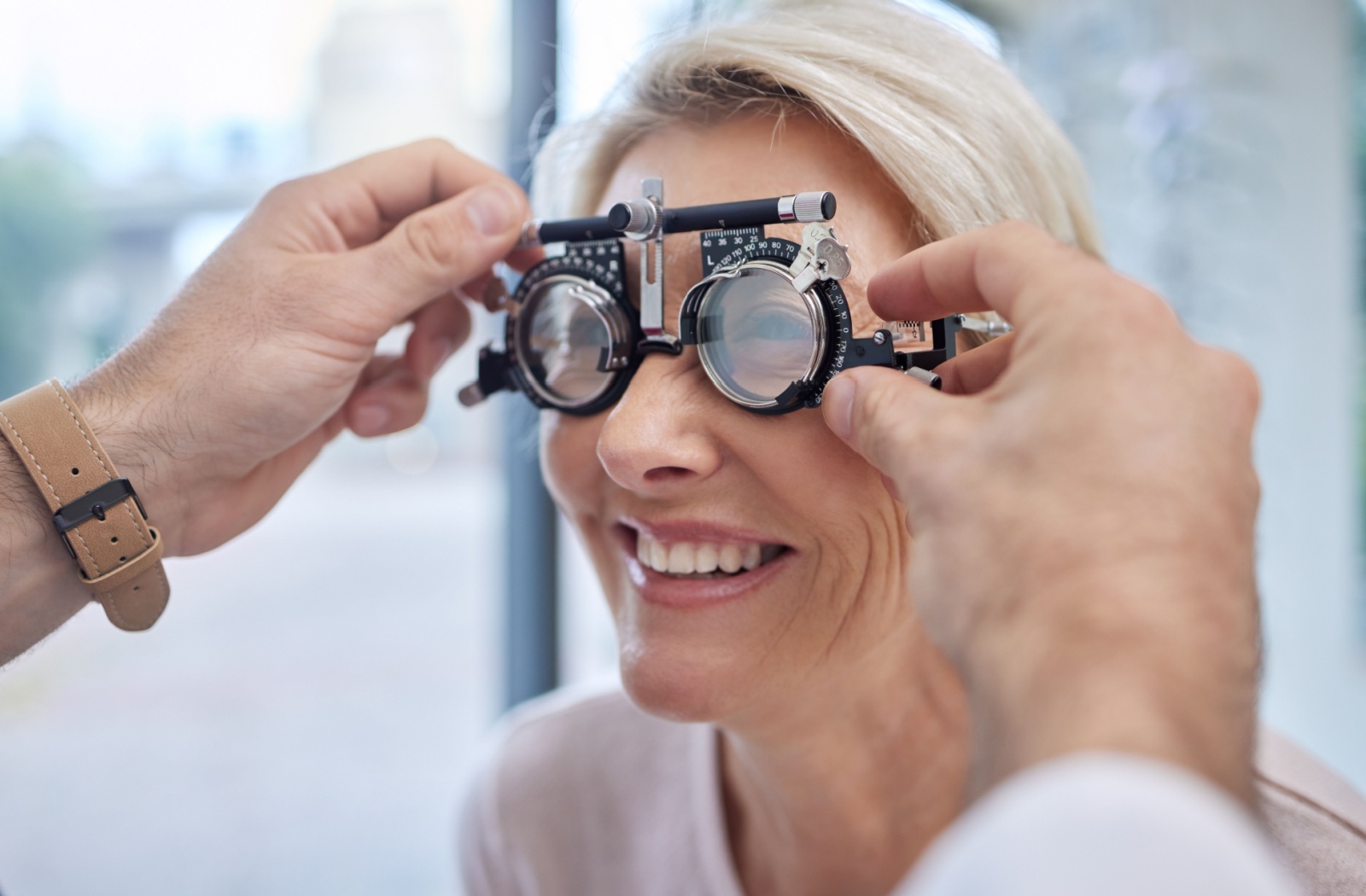 A person smiles while wearing a trial frame during an eye exam.