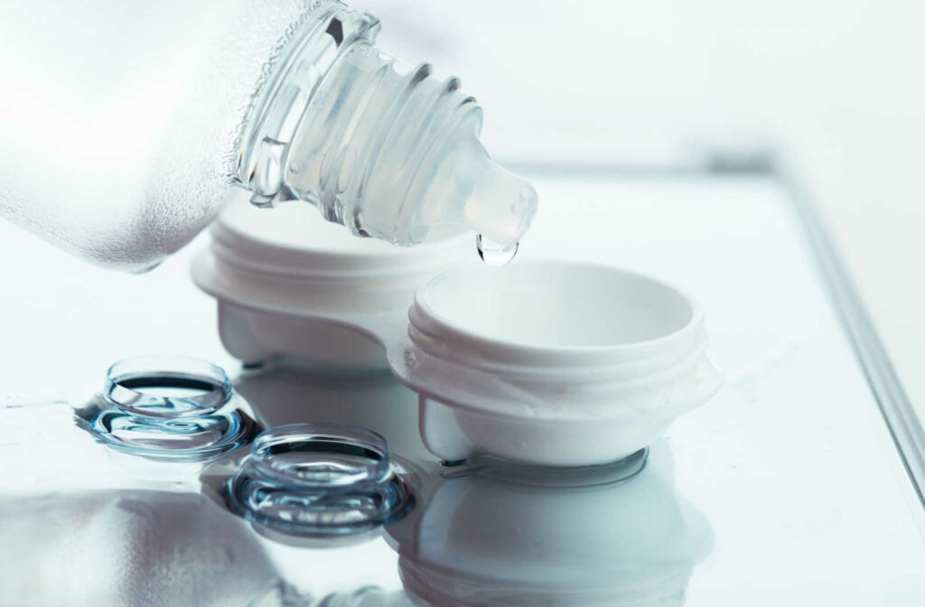 Contact lens solution being dripped into a contact lens case with two contact lenses sitting in front.