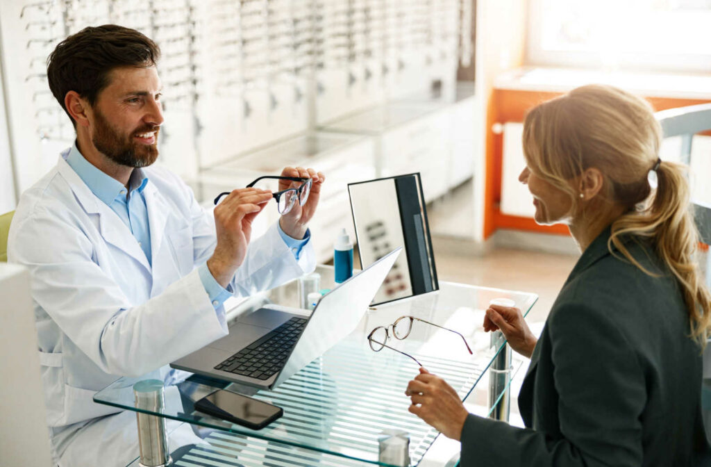 An optician sitting across from a patient helping to fit the perfect pair of eyeglasses.