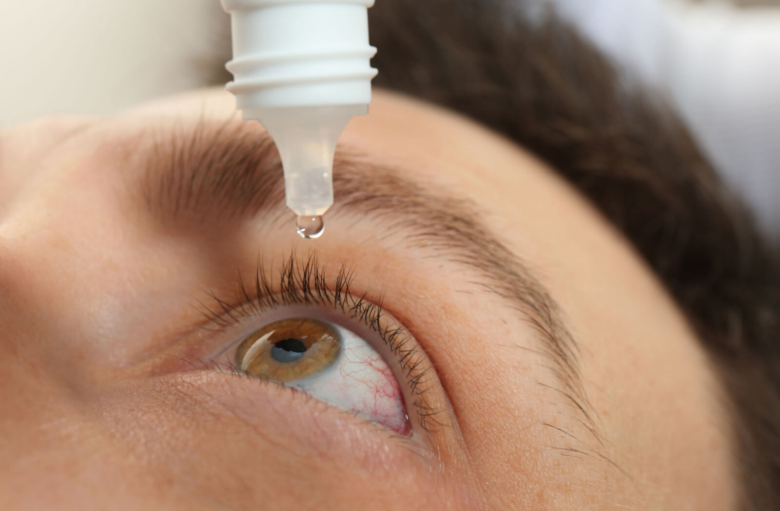 Close up shot of a man's head tilted back while putting a drop of Lumify eye drops.