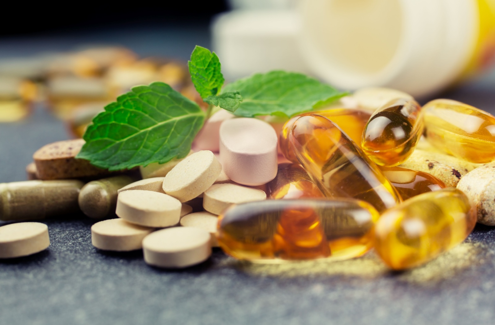 A closeup of several vitamins and supplements spilling out of a container