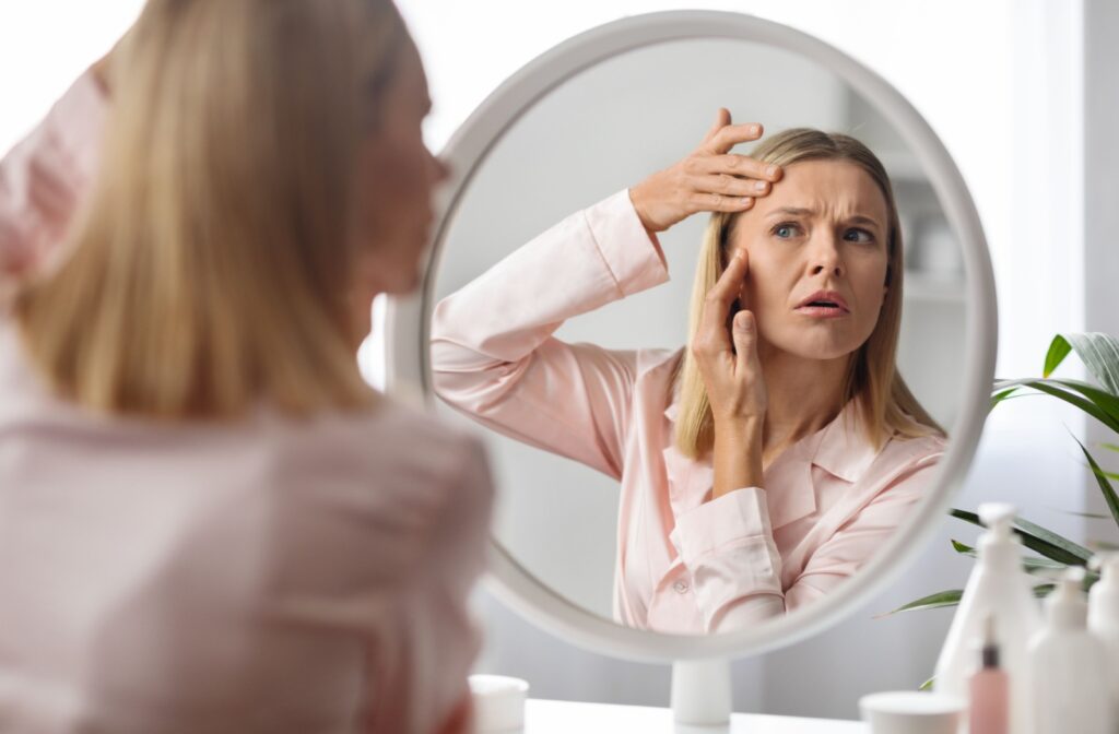 A concerned middle-aged woman examines dry skin around her eyes in a mirror