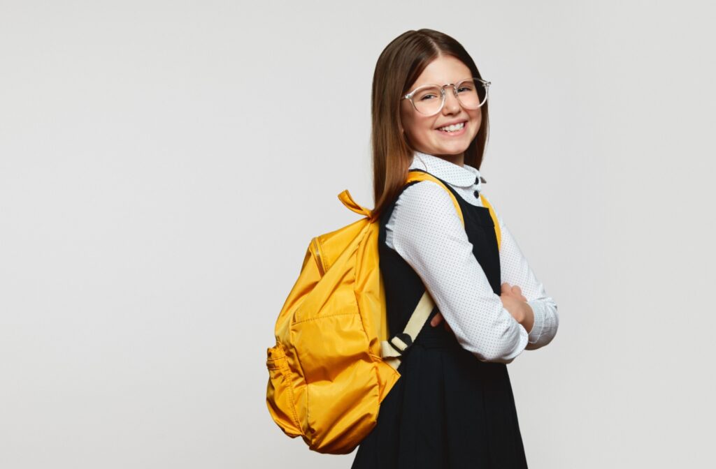 A side view of a smiling girl with eyeglasses wearing a yellow backpack.