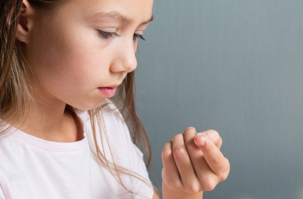 A school-aged child looking down at a contact lens resting on their left index finger.