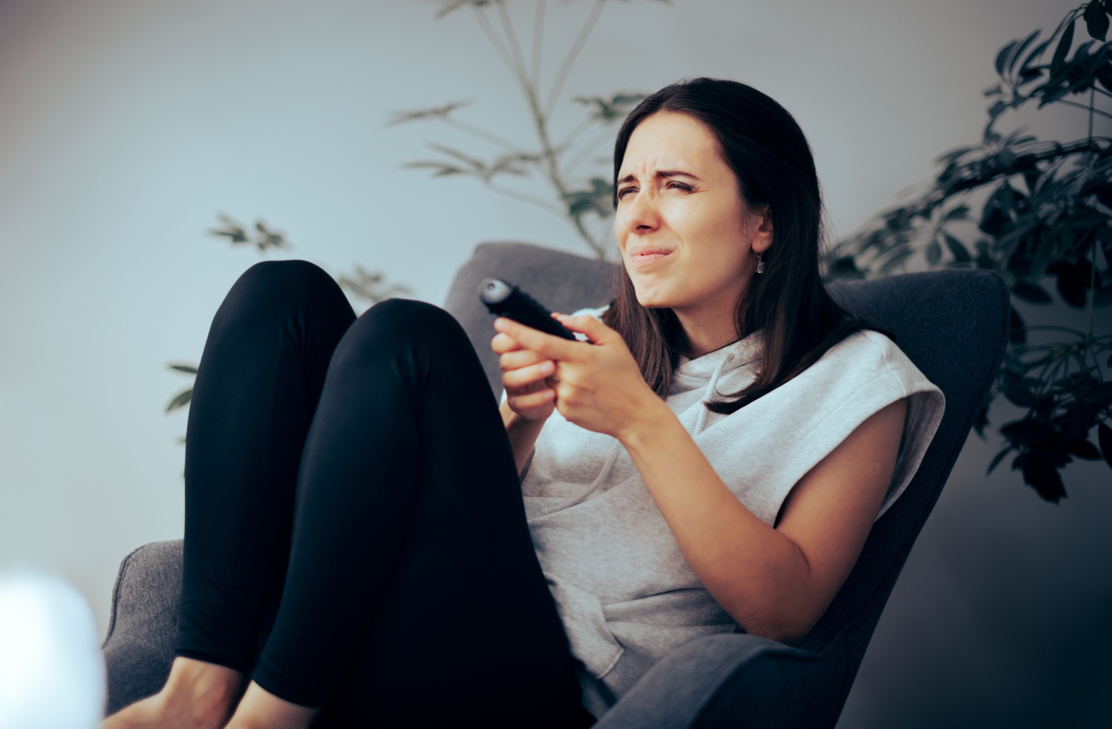 A person holds the remote for their TV while squinting at the distant screen.