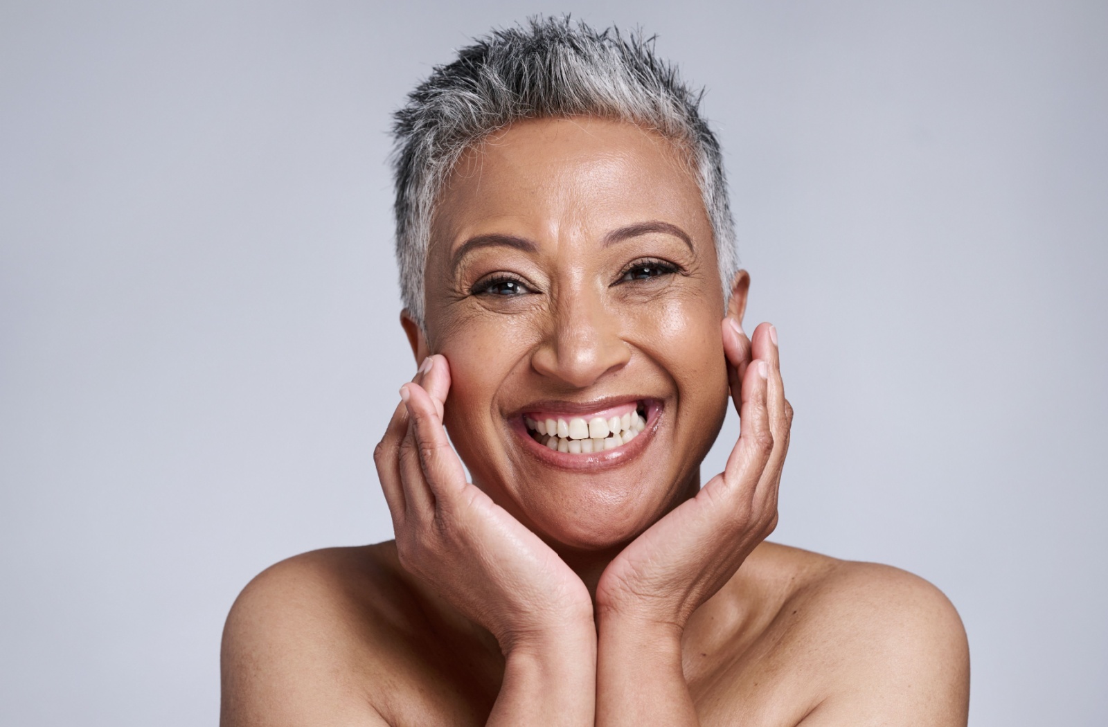 A smiling older adult with short gray hair looks directly at the camera, showcasing their clear, smooth skin after successfully treating acne scars.