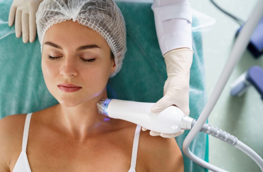 A calm individual with dark hair secured in a hairnet sits comfortably in a treatment chair as an RF laser gently treats their skin.