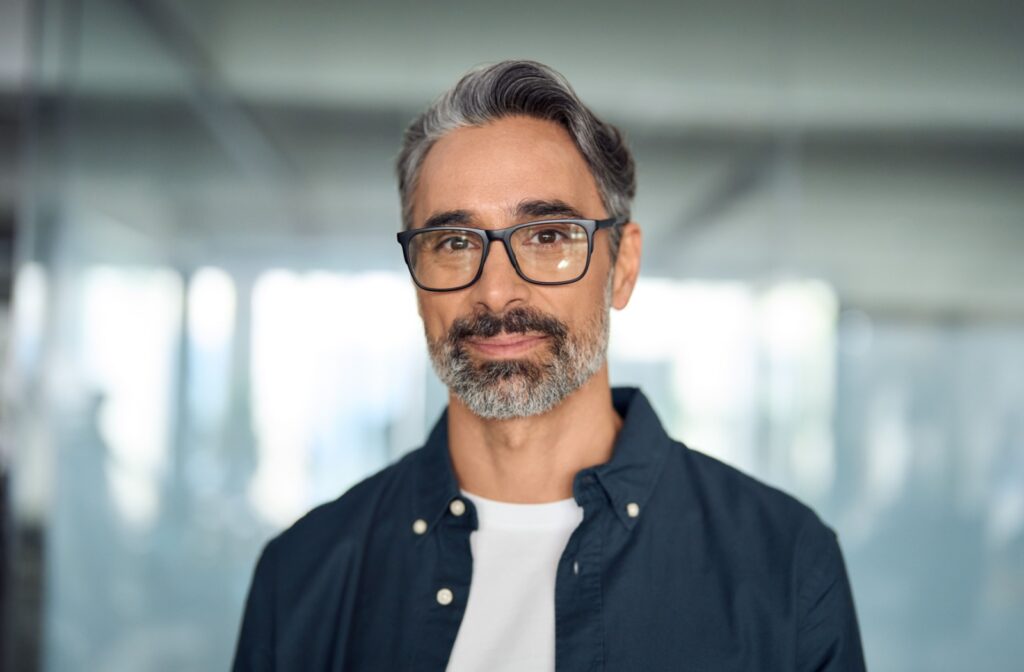 A mature-looking person smiles at the camera, sporting black-rimmed glasses.