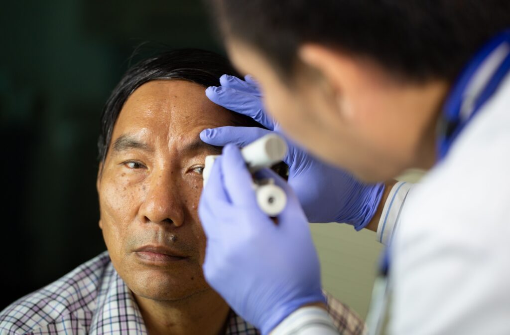 An optometrist shines a light into a patient’s eye as part of a comprehensive eye exam to check for concerns of AMD.
