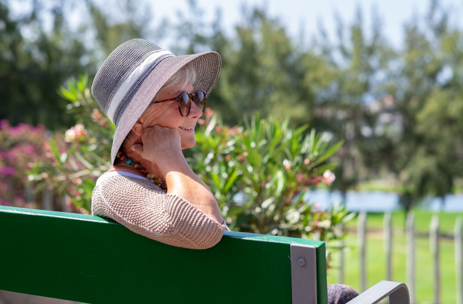 A senior wearing sunglasses sits on a bench to enjoy the outdoors while protecting their eyes to reduce AMD risks.