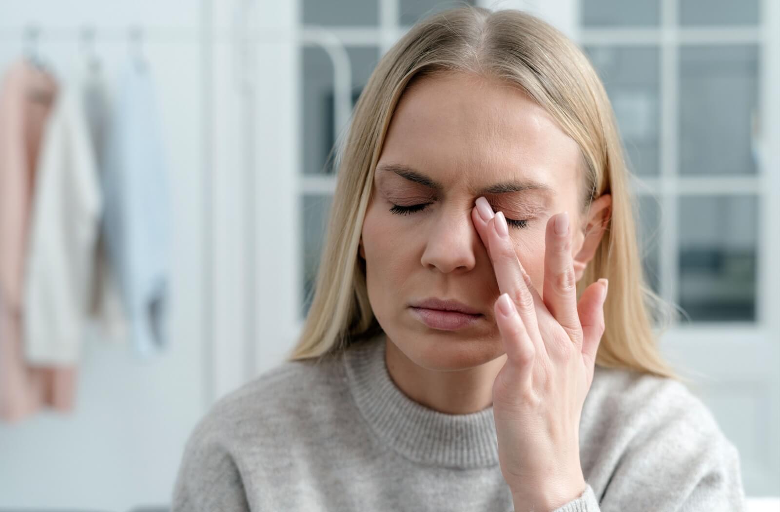 A person with their eyes closed rubbing their left eye due to meibomian gland discomfort.