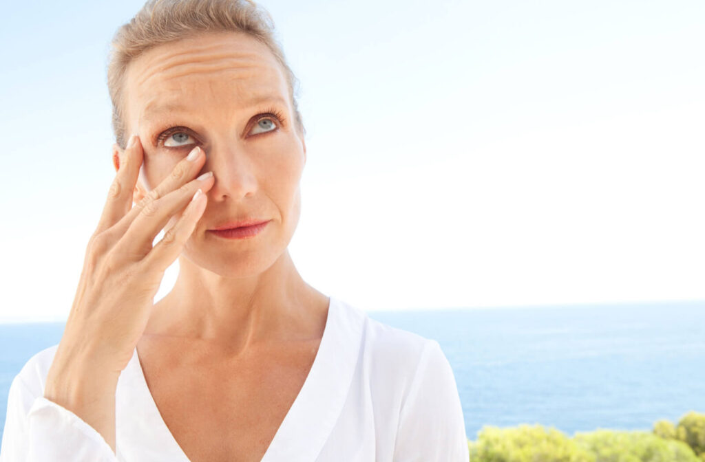 A woman in a white colored blouse with her eyes getting dry while she is outside near the beachfront.