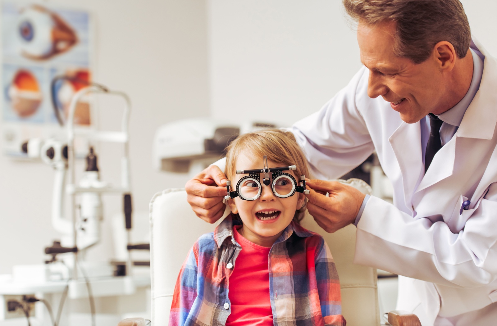 An eye doctor adjusting the lens tool on a young child during their annual eye exam.