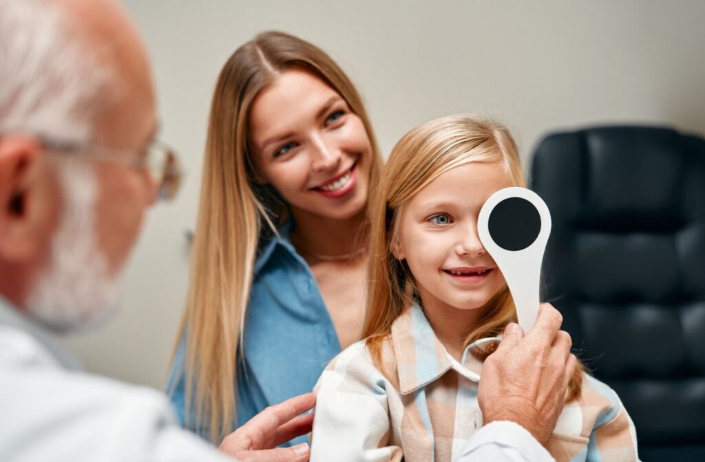 An eye doctor covering a child's left eye during a visual assessment at the child's annual routine eye exam visit.
