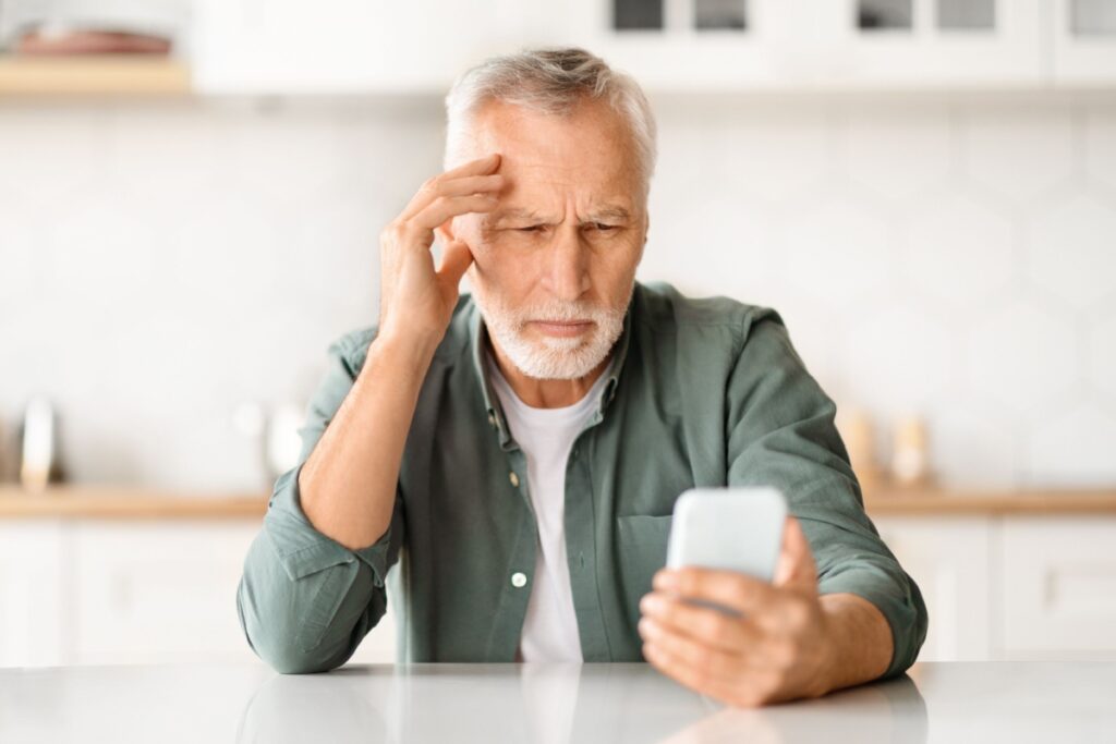 An older man holding a phone farther away to see clearly, a common sign of presbyopia and reduced near focusing ability.