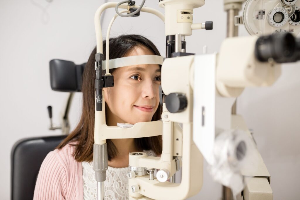 Young woman positioned at slit lamp equipment during thorough eye examination with optometrist.